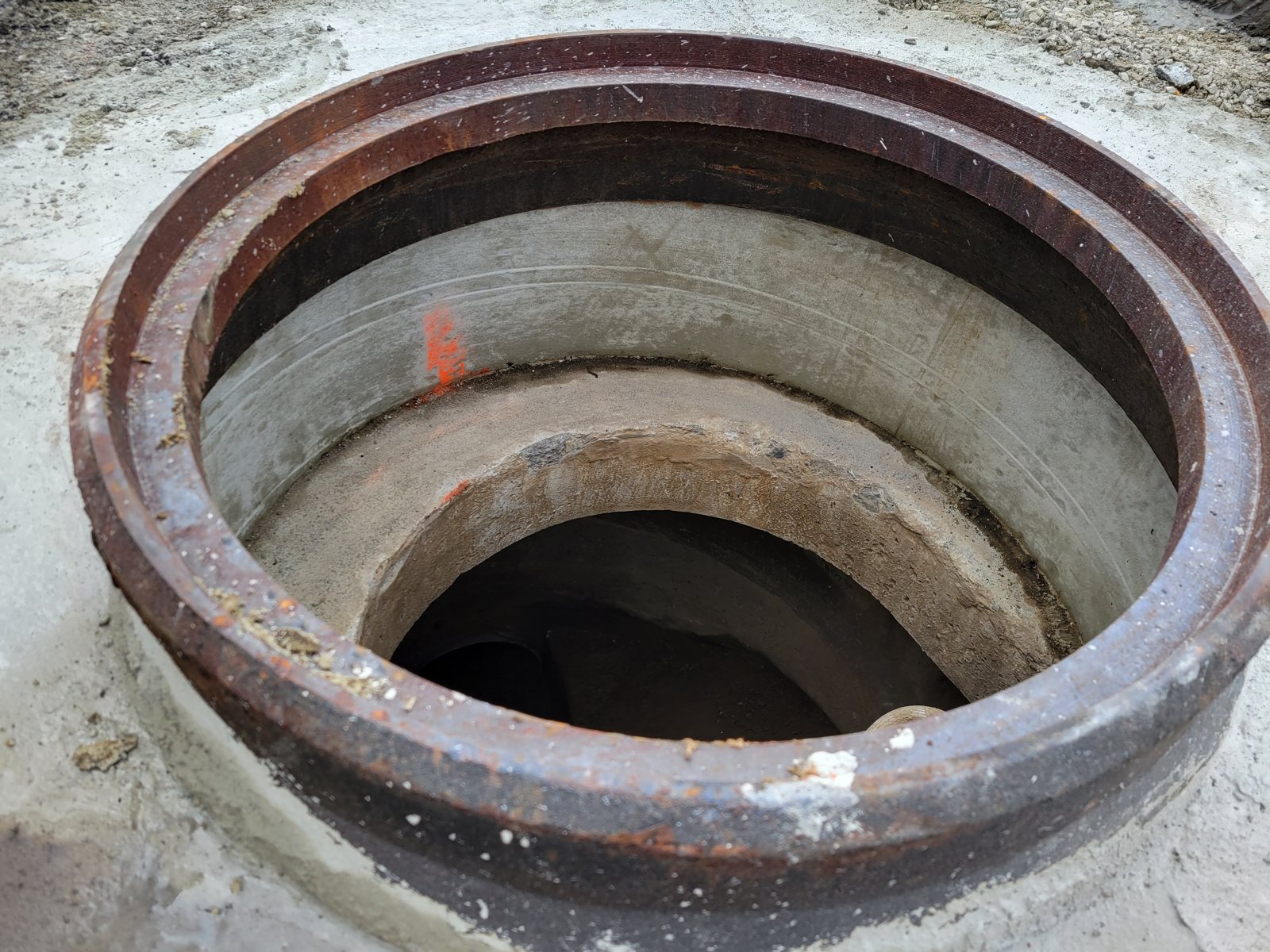 Looking down into a rebuilt manhole: the frame set in one smooth, solid concrete chimney with no rings or seams