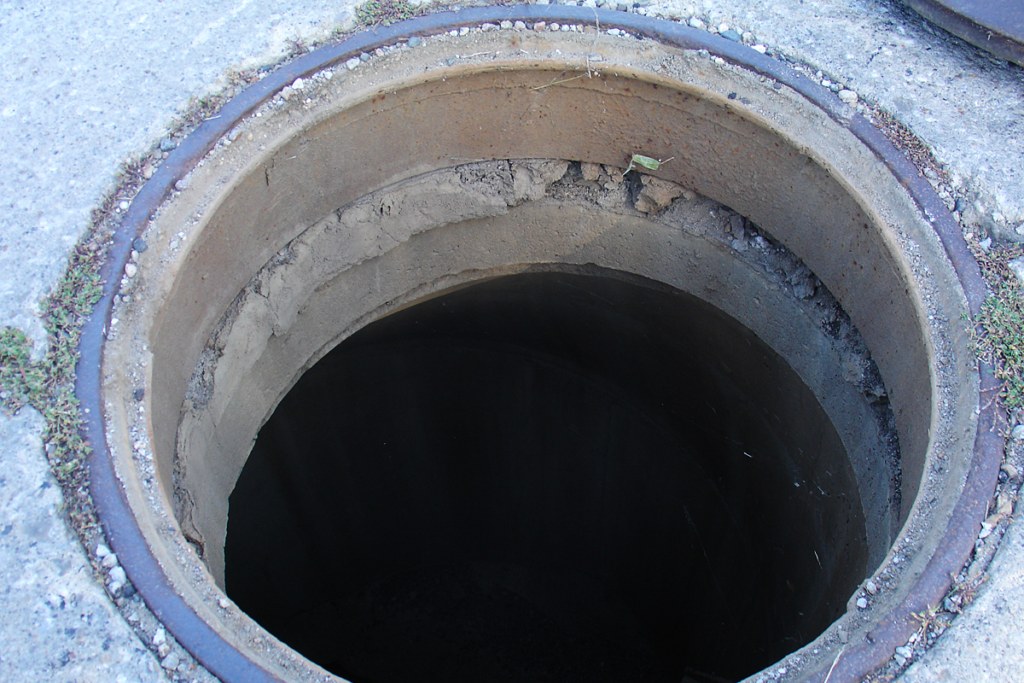 Open manhole showing stacked riser rings with cracked, crumbling grout between them