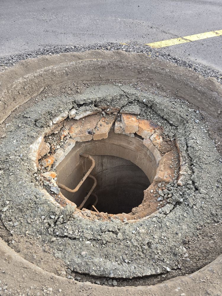 Open manhole with broken, crumbling riser rings around the chimney