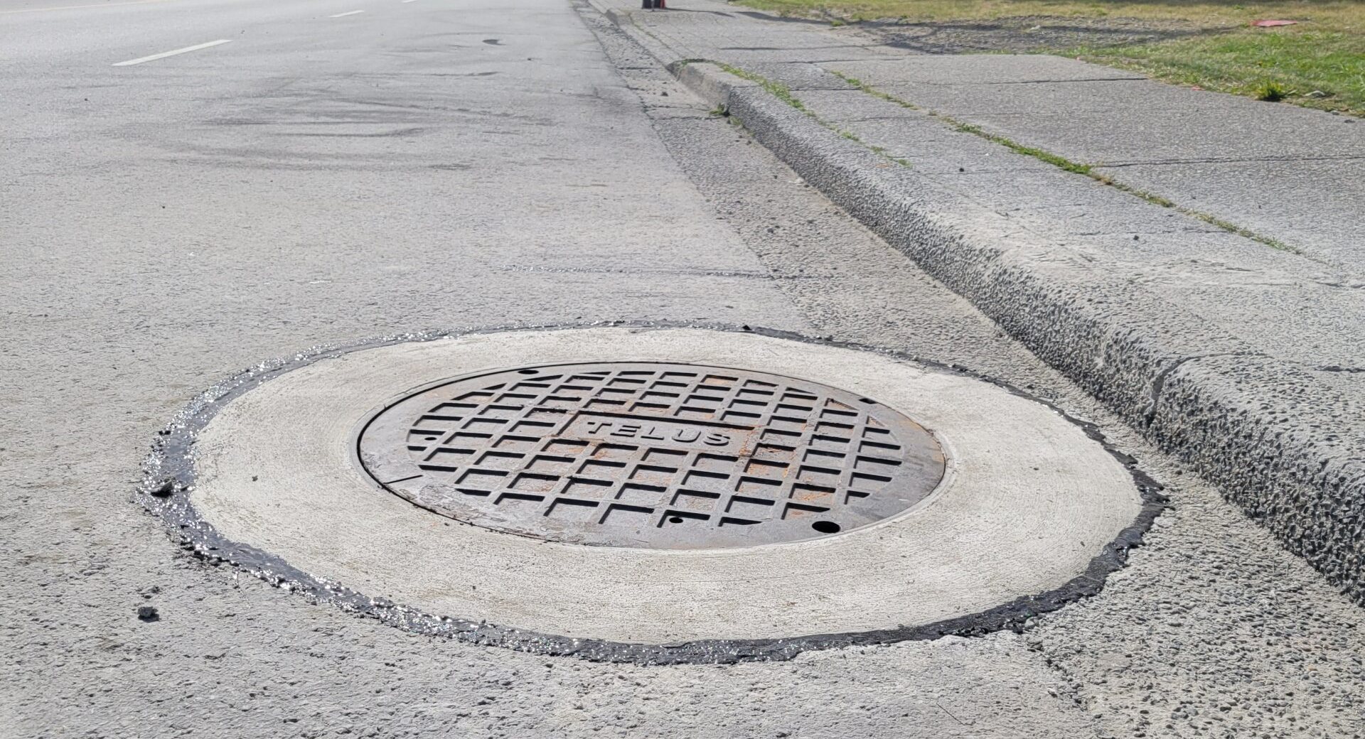 Finished manhole with a round concrete collar set flush in a city street, traffic in the distance